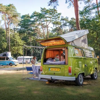 Kamperen bij Huttopia met retro camper, familie die ontspant onder de bomen en een natuurlijke bosrijke omgeving.